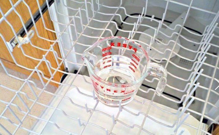 Glass measuring cup filled with white vinegar placed  in the dishwasher top rack
