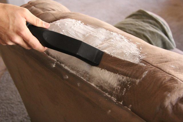 Baking soda being vacuumed from a dark brown couch