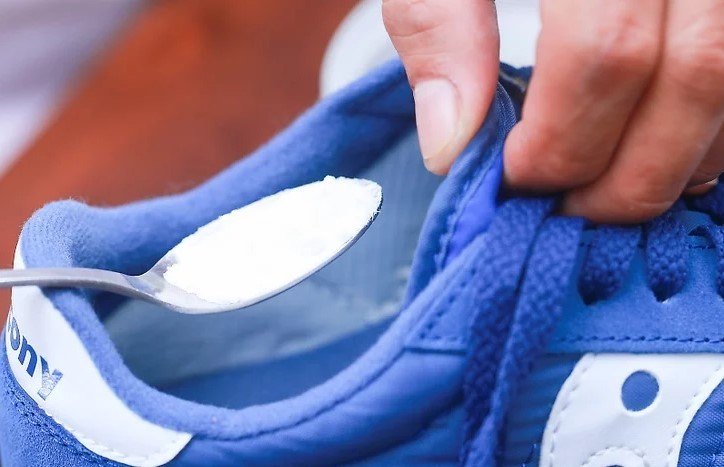 Baking soda being poured inside a tennis shoe with a spoon