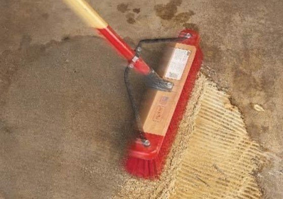 Floor with solution on top of the oil stain being brushed with a red brush